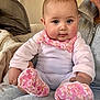 baby, infant, child, adult_partial, face, blue_eyes, chubby_cheeks, bib, floral_pattern, pink, onesie, booties, sitting, lap, blanket, indoor, portrait, smile, caregiver, cozy