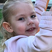 Olivia joined the competition — help win amazing prizes! background, blonde_hair, casual_clothing, child, daylight, face, happy, holding, light_pink, nature, outdoor, park, person, playground, pole, smile, sweatshirt, tree, vehicle, young_child
