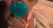 Elianna is registered to the contest to win money with this photo: baby, infant, pacifier, curly_hair, clothing, arm, person, cute, closeup, face, hand, indoor, blanket, pink, soft_toys, newborn, sleepwear, child, resting, portrait