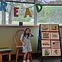 animal_illustrations, carpet, chair, child, classroom, display_board, dress, educational, girl, indoor, letters, library, nature_outside, pink_shoes, playful, poster, reading_area, smiling, window, wooden_furniture