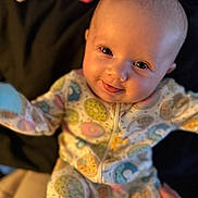 Thea is registered to the contest to win money with this photo: baby, infant, smiling, pajamas, donut_pattern, cute, face, eyes, hands, soft_lighting, cozy, background, child, person, apparel, sleepwear, portrait, young, happy, indoor