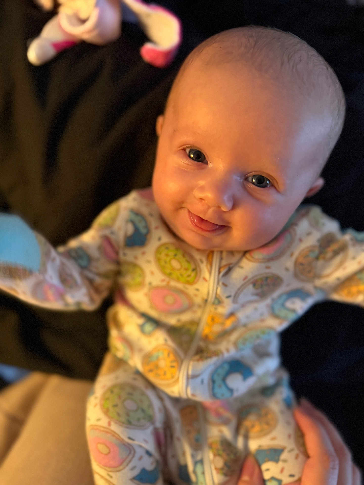 Thea is registered to the contest to win money with this photo: baby, infant, smiling, pajamas, donut_pattern, cute, face, eyes, hands, soft_lighting, cozy, background, child, person, apparel, sleepwear, portrait, young, happy, indoor