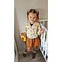 child, girl, pigtails, hair_clips, flower_pattern, cardigan, skirt, socks, sunflower_purse, indoor, crib, wooden_floor, smile, pose, cute, fashion, playful, light_skin, blue_eyes, home