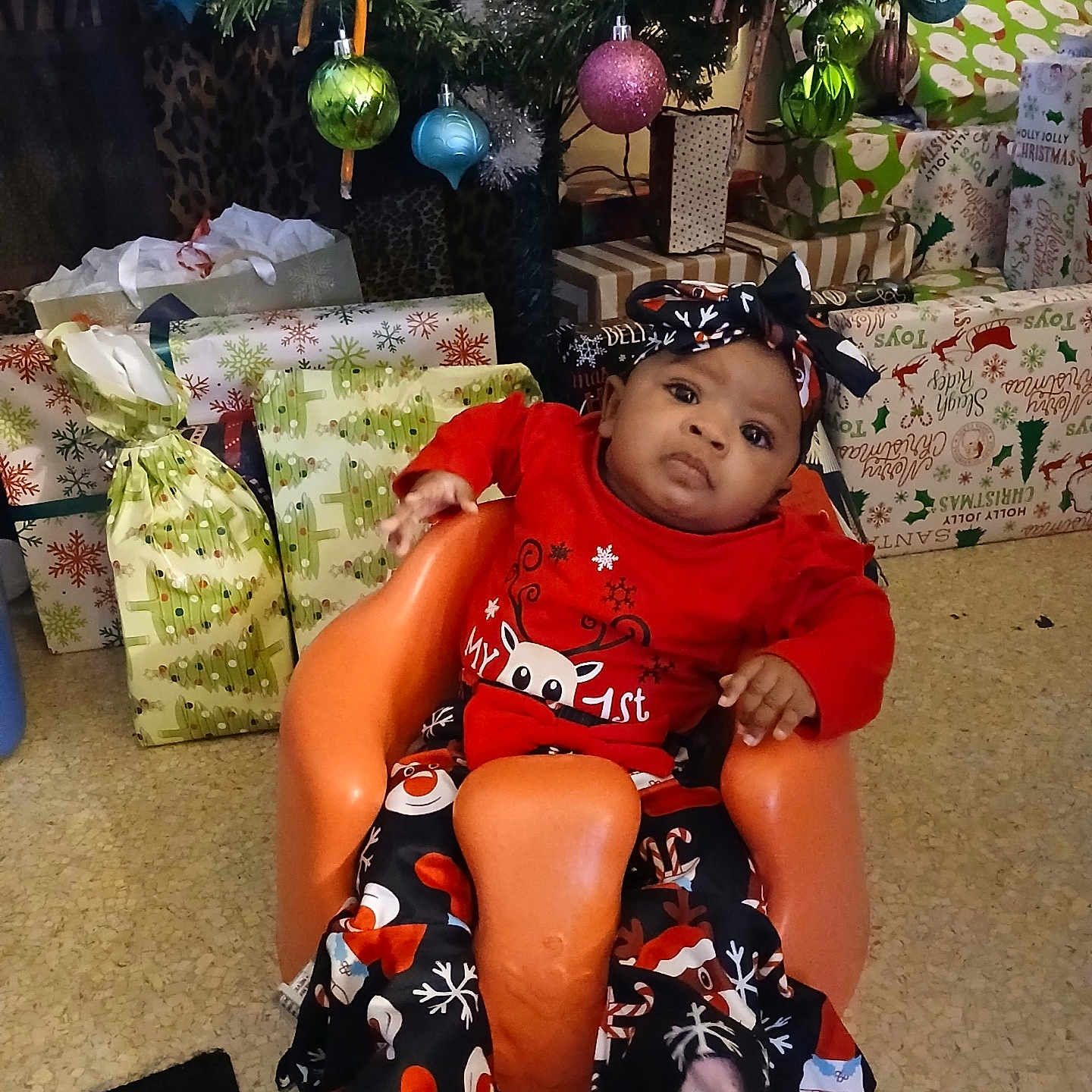 Za'Nyla is registered to the contest to win money with this photo: baby, celebration, child, christmas_tree, cute, decorations, family, festive, floor, headband, holiday_clothing, holiday_season, indoor, infant, orange_seat, portrait, presents, seasonal, smiling, wrapped_gifts