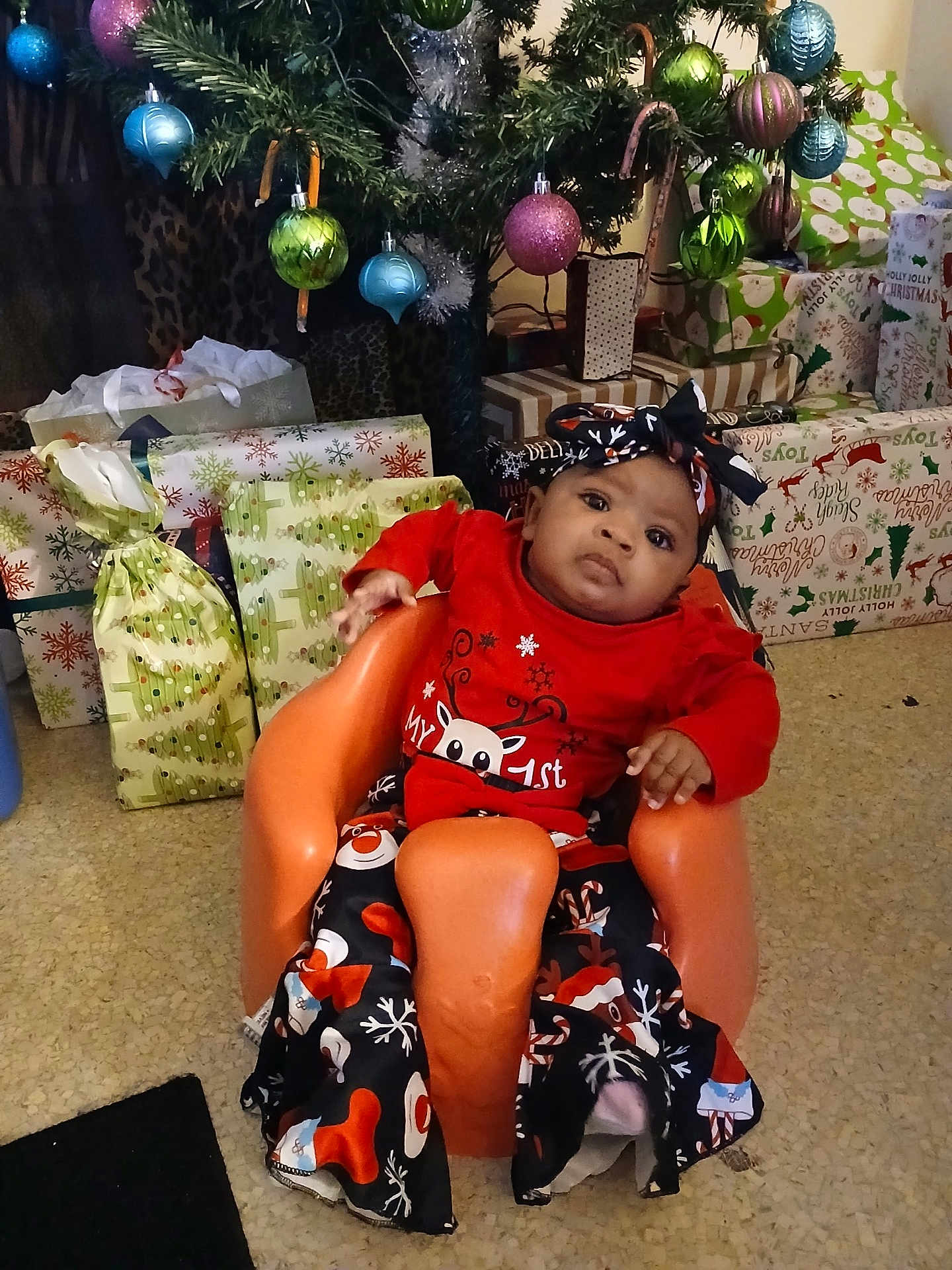 Za'Nyla is registered to the contest to win money with this photo: baby, child, christmas_tree, presents, holiday_clothing, orange_seat, festive, indoor, headband, floor, decorations, wrapped_gifts, holiday_season, infant, cute, portrait, celebration, smiling, family, seasonal