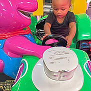 Za'Nyla is registered to the contest to win money with this photo: toddler, child, arcade, kiddie_ride, steering_wheel, purple_character, green, pink, toy, playful, indoor, amusement, young_child, person, bright_colors, fun, cute, entertainment, hands, focused