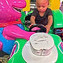 toddler, child, arcade, kiddie_ride, steering_wheel, purple_character, green, pink, toy, playful, indoor, amusement, young_child, person, bright_colors, fun, cute, entertainment, hands, focused