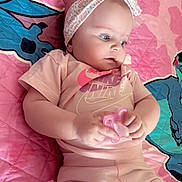 Ariana a rejoint le concours — aidez-le/la à gagner de superbes lots ! baby, child, clothing, colorful_background, comfortable, cute, headband, indoor, infant, looking_away, lying_down, pacifier, patterned_headband, pink_clothing, portrait, quilt, relaxed, small_hands, soft_lighting, toddler