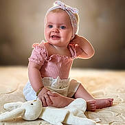 Ariana is registered to the contest to win money with this photo: baby, child, smiling, pink_clothing, headband, bracelet, plush_toy, white_bunny, blanket, sitting, indoors, cute, happy, portrait, infant, soft_lighting, young_child, playful, comfortable, adorable