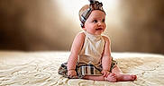 Ariana is registered to the contest to win money with this photo: baby, barefoot, blanket, child, clothing, cute, expression, happy, headband, indoor, infant, person, plaid, portrait, sitting, skirt, smiling, soft_light, texture, young