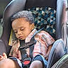 boy, car_seat, car_window, casual_clothing, child, curly_hair, denim_shorts, indoors, peaceful, plaid_shirt, portrait, relaxed, resting, safety_harness, seat_padding, seatbelt, sleeping, toddler, vehicle_interior, young_child