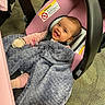 baby, infant, child, smiling, car_seat, stroller, blanket, pink, gray, cozy, portrait, indoor, carpet, seated, clothing, gloves, pacifier, happy, face, photograph