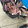 baby, infant, child, car_seat, stroller, pink_blanket, pacifier, smiling, face, portrait, adult, tattoos, arm, sneakers, shoes, outdoor, concrete, floor, family, casual