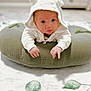 baby, infant, hoodie, white_clothing, cushion, green_cushion, lying_down, face, hands, curious, indoors, carpet, blurred_background, cute, child, soft_lighting, baby_boy, baby_girl, hood_with_ears, person