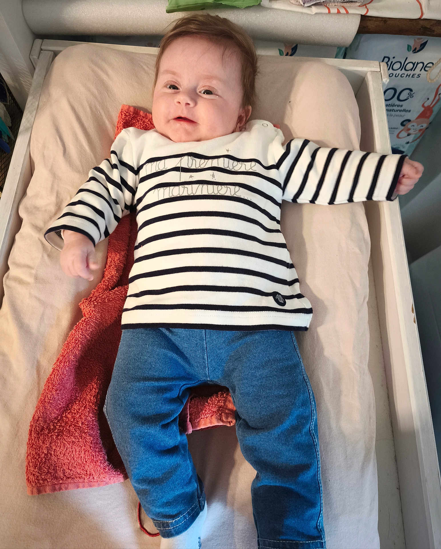 Athénaïs a rejoint le concours — aidez-le/la à gagner de superbes lots ! baby, baby_clothes, blue_pants, changing_pad, child, clothing, cute, expression, face, furniture, happy, head, indoor, infant, lying_down, person, smiling, striped_shirt, toddler, towel