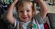 Celica joined the competition — help win amazing prizes! cartoon_shirt, chair, child, clothing, eyes, face, flowers, gray_shirt, hair, hat, home, indoors, photography, playful, portrait, raised_arms, seated, shelves, smiling, toddler