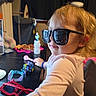 Celica joined the competition — help win amazing prizes! child, toddler, sunglasses, portrait, indoors, sitting, table, toy, pink, blonde_hair, smiling, side_profile, casual_clothing, playtime, home, furniture, bracelet, black_table, camera, funny_pose