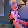 Wren is registered to the contest to win money with this photo: baby, child, infant, portrait, sitting, held, adult, lap, face, wide_eyed, indoor, home, lamp, lighting, colorful, purple_light, onesie, watch, window, furniture
