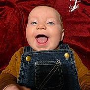 Wren joined the competition — help win amazing prizes! baby, infant, child, portrait, smiling, happy, open_mouth, blue_eyes, face, head, overalls, denim, mustard_shirt, red_background, blanket, lying_down, closeup, indoors, photography, adorable