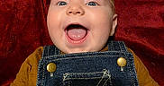 Wren joined the competition — help win amazing prizes! baby, infant, child, portrait, smiling, happy, open_mouth, blue_eyes, face, head, overalls, denim, mustard_shirt, red_background, blanket, lying_down, closeup, indoors, photography, adorable