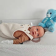 Alistair is registered to the contest to win money with this photo: baby, infant, changing_table, teddy_bear, blue_toy, soft_toy, cute, cozy, neutral_colors, child, laying_down, clothing, face, indoor, baby_garment, toy, portrait, looking_away, fabric, bedroom