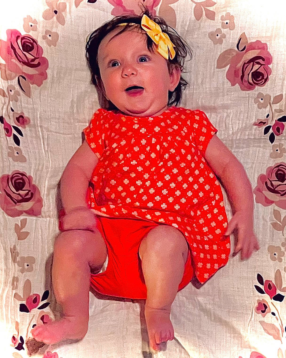 Julia is registered to the contest to win money with this photo: arm, baby, baby_toddler_clothing, child, dress, face, facial_expression, happy, head, magenta, pattern, person, petal, pink, red, skin, sleeve, sun_hat, textile, toddler