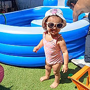 Inaya participe au concours pour gagner de l'argent avec cette photo : toddler, child, swimsuit, sunglasses, hat, barefoot, grass, inflatable_pool, summer, sunlight, outdoor, man, adult, backyard, water, toy, blue, pink, shadow, play