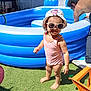 toddler, child, swimsuit, sunglasses, hat, barefoot, grass, inflatable_pool, summer, sunlight, outdoor, man, adult, backyard, water, toy, blue, pink, shadow, play