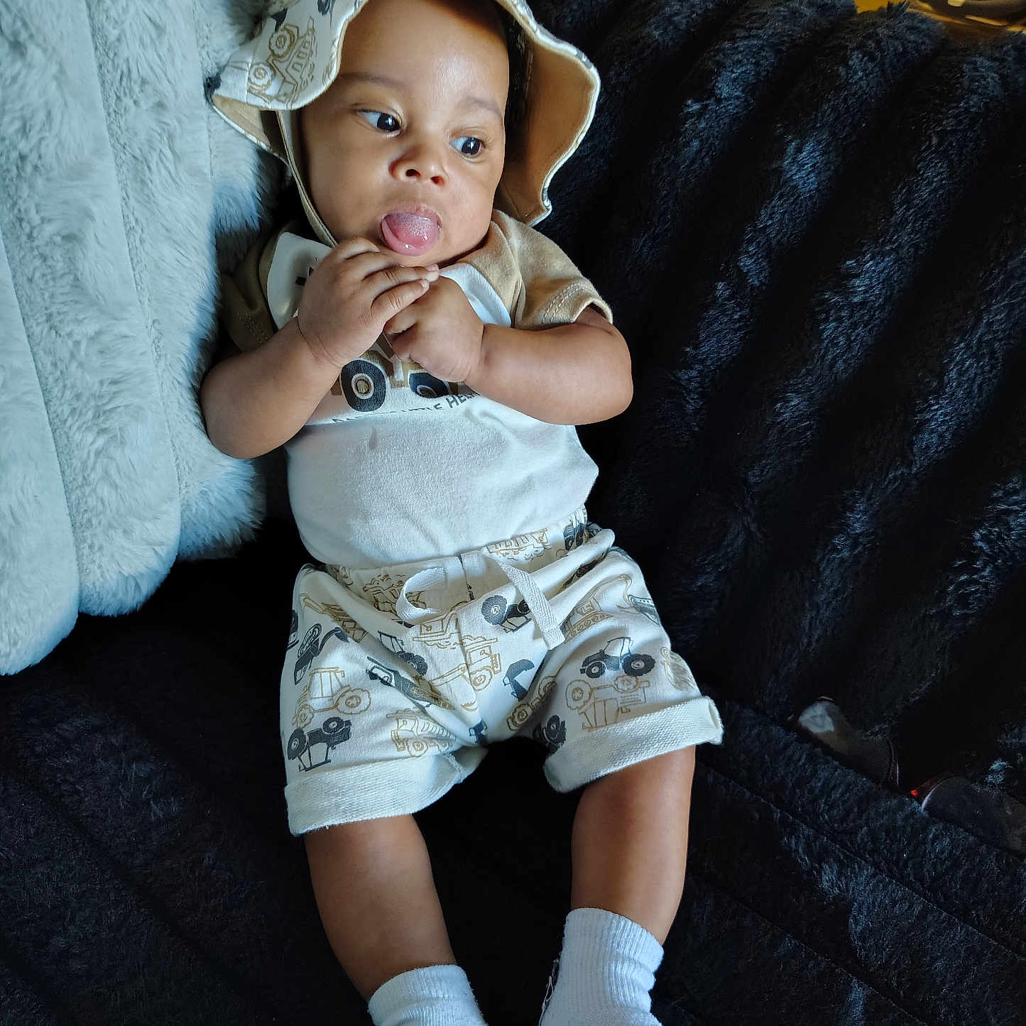 Kai'Mauri joined the competition — help win amazing prizes! baby, child, hat, socks, shorts, tshirt, couch, blanket, indoor, person, tongue_out, playful, cute, clothing, infant, seated, smiling, furniture, relaxed, home