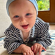 Lily is registered to the contest to win money with this photo: baby, infant, crawling, smiling, striped_clothing, blue_hat, carpet, indoor, face, hands, cute, child, happy, person, floor, home, playing, bright_eyes, closeup, natural_light