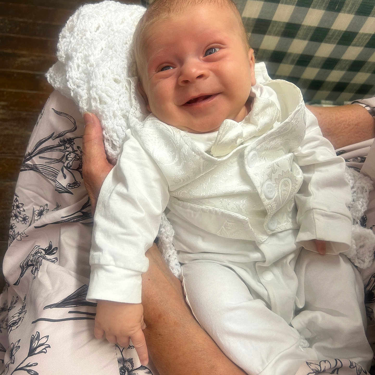 Hudson is registered to the contest to win money with this photo: baby, infant, smile, white_clothing, knitted_blanket, adult_hand, floral_pattern, fabric, happy, portrait, indoor, wooden_floor, cute, newborn, person, face, holding, comfort, cozy, soft_lighting