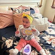 Phoenix joined the competition — help win amazing prizes! baby, child, smiling, headband, yellow, pink_leggings, white_socks, bed, pillows, floral_bedspread, bottle, baby_lotion, indoor, happy, person, cute, playful, clothing, sitting, room