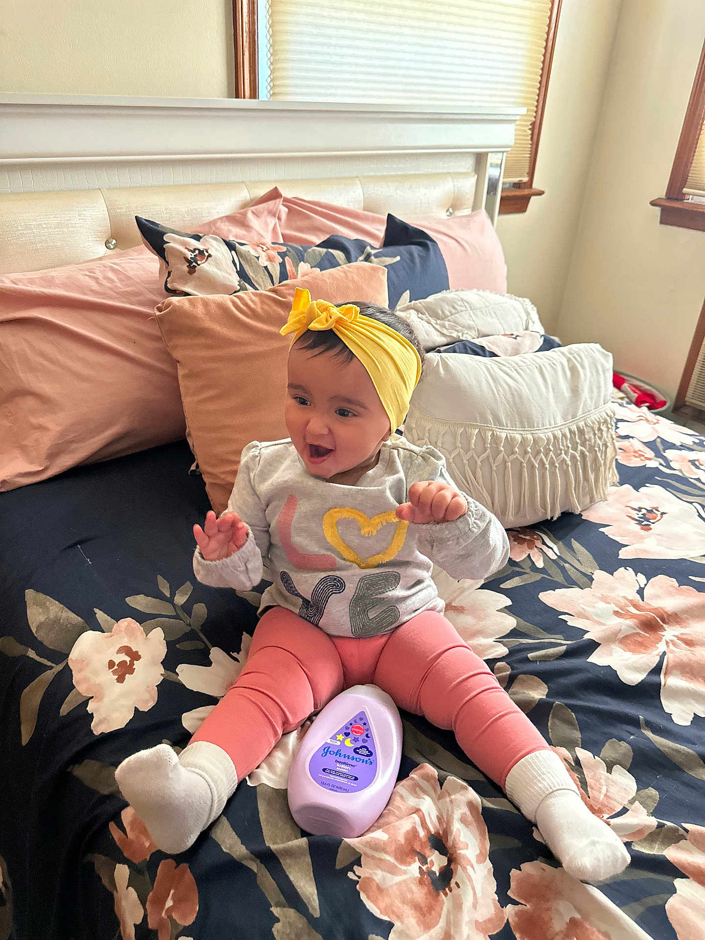 Phoenix joined the competition — help win amazing prizes! baby, child, smiling, headband, yellow, pink_leggings, white_socks, bed, pillows, floral_bedspread, bottle, baby_lotion, indoor, happy, person, cute, playful, clothing, sitting, room