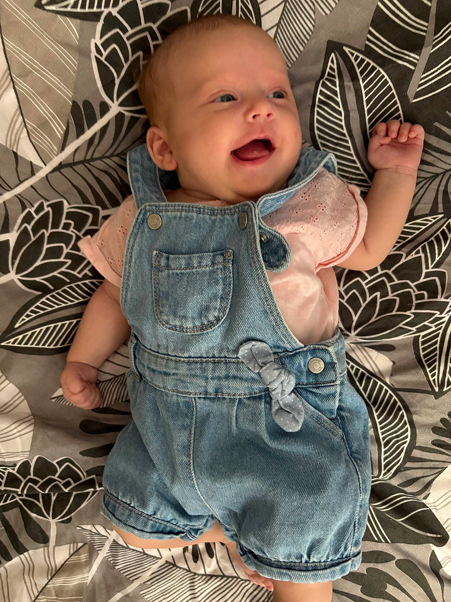 Esmée a rejoint le concours — aidez-le/la à gagner de superbes lots ! baby, infant, smiling, denim_overalls, pink_shirt, lying_down, patterned_blanket, happy, cute, child, face, small_baby, clothing, portrait, closeup, person, skin, head, hand, expression