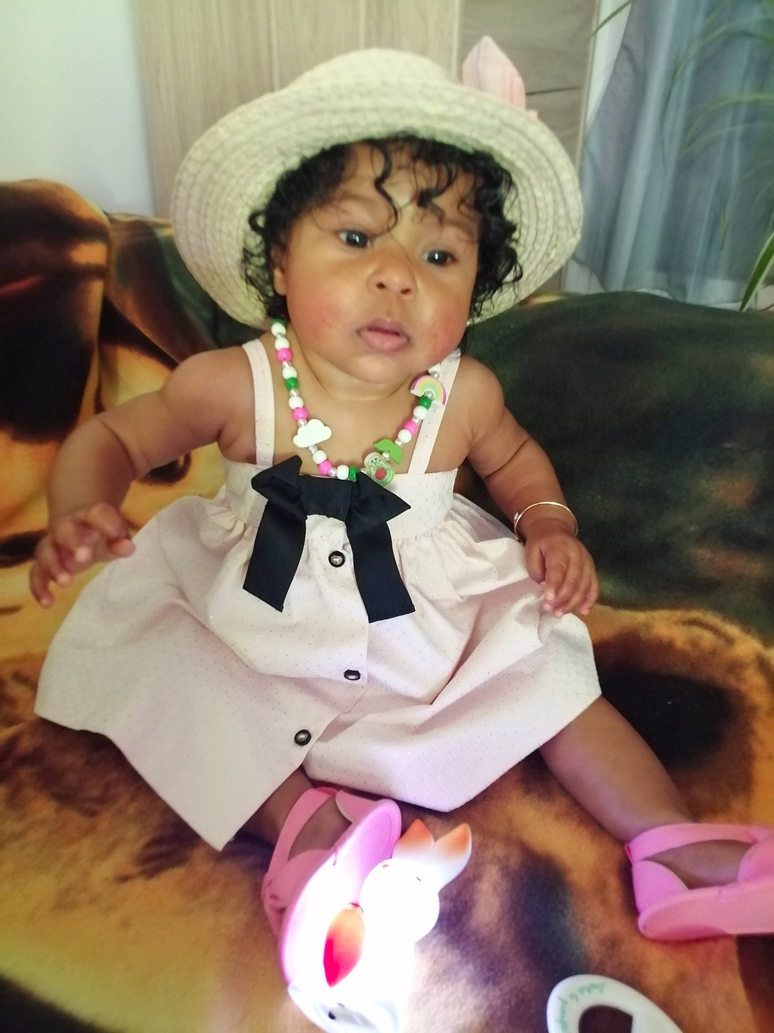 Safia participe au concours pour gagner de l'argent avec cette photo : baby, baby_products, baby_toddler_clothing, bow_tie, child, coffee_cup, curtain, event, fashion_accessory, formal_wear, fun, happy, hat, person, pink, room, sitting, sock, sun_hat, toddler