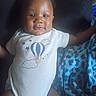 Dakari is registered to the contest to win money with this photo: baby, infant, child, portrait, sitting, car_seat, onesie, clothing, hot_air_balloon, blanket, blue, face, eyes, hair, indoor, vehicle, adult_arm, candid, close_up, photography