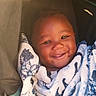 Dakari is registered to the contest to win money with this photo: baby, child, infant, smiling, portrait, blanket, cozy, indoor, seated, face, eyes, hair, happy, cute, closeup, soft_lighting, warm_tones, textile, bedding, photography