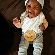 Jeremiah Phillips is registered to the contest to win money with this photo: baby, bib, brown_couch, celebration, child, couch, cozy_clothing, cute, feet, happy, hat, indoor, infant, milestone, person, portrait, sitting, smiling, socks, wooden_sign