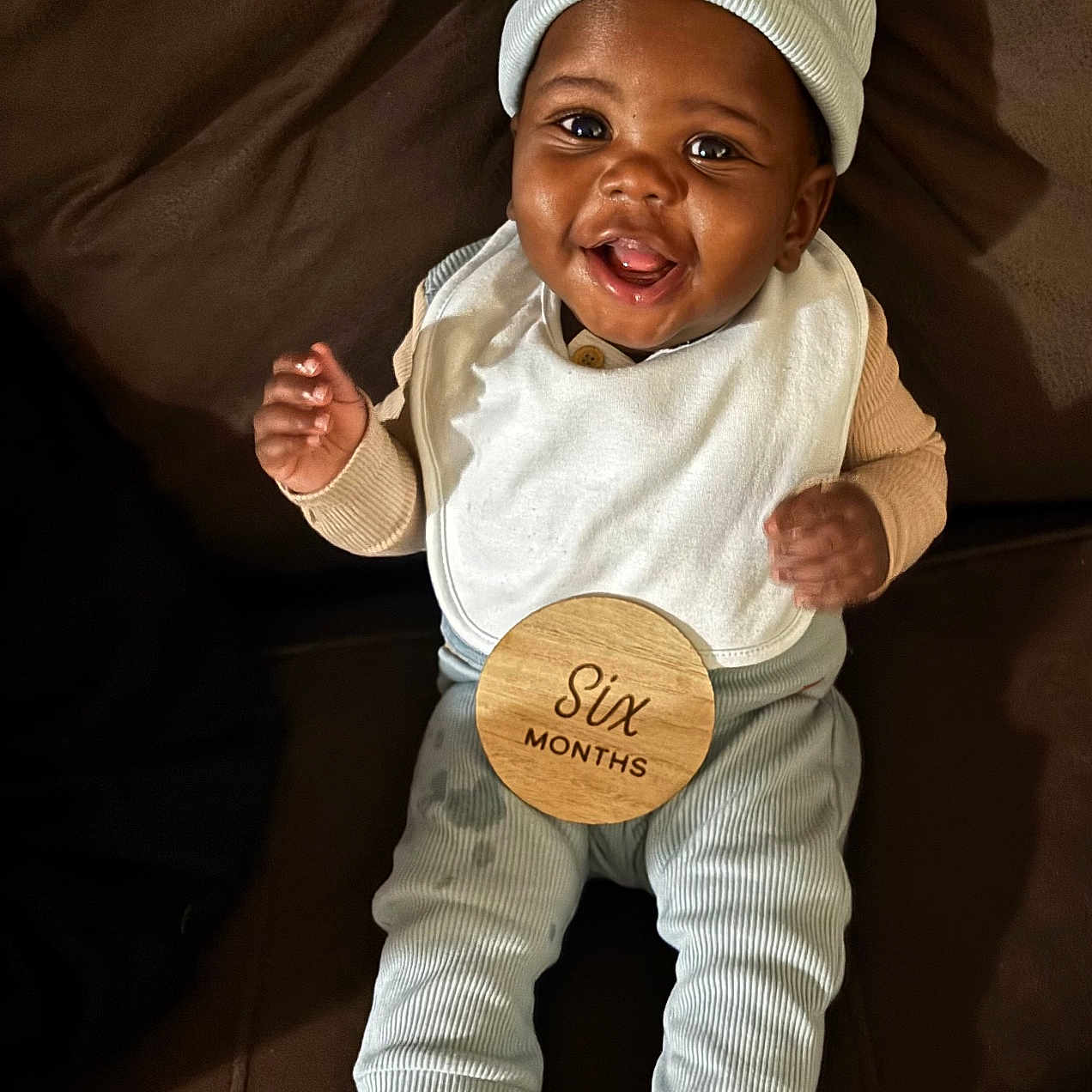 Jeremiah Phillips is registered to the contest to win money with this photo: baby, bib, brown_couch, celebration, child, couch, cozy_clothing, cute, feet, happy, hat, indoor, infant, milestone, person, portrait, sitting, smiling, socks, wooden_sign