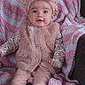 baby, infant, child, portrait, sitting, smiling, wide_eyed, pink_outfit, headband, bow, fluffy_vest, blanket, striped_blanket, couch, socks, clothing, indoors, cozy, face, photography