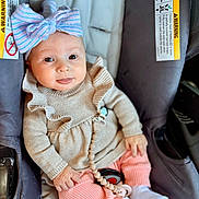 Viviana is registered to the contest to win money with this photo: baby, child, car_seat, bow, smile, pink_pants, beige_sweater, white_socks, infant, cute, happy, seated, indoors, clothing, face, hand, toy, accessory, portrait, person