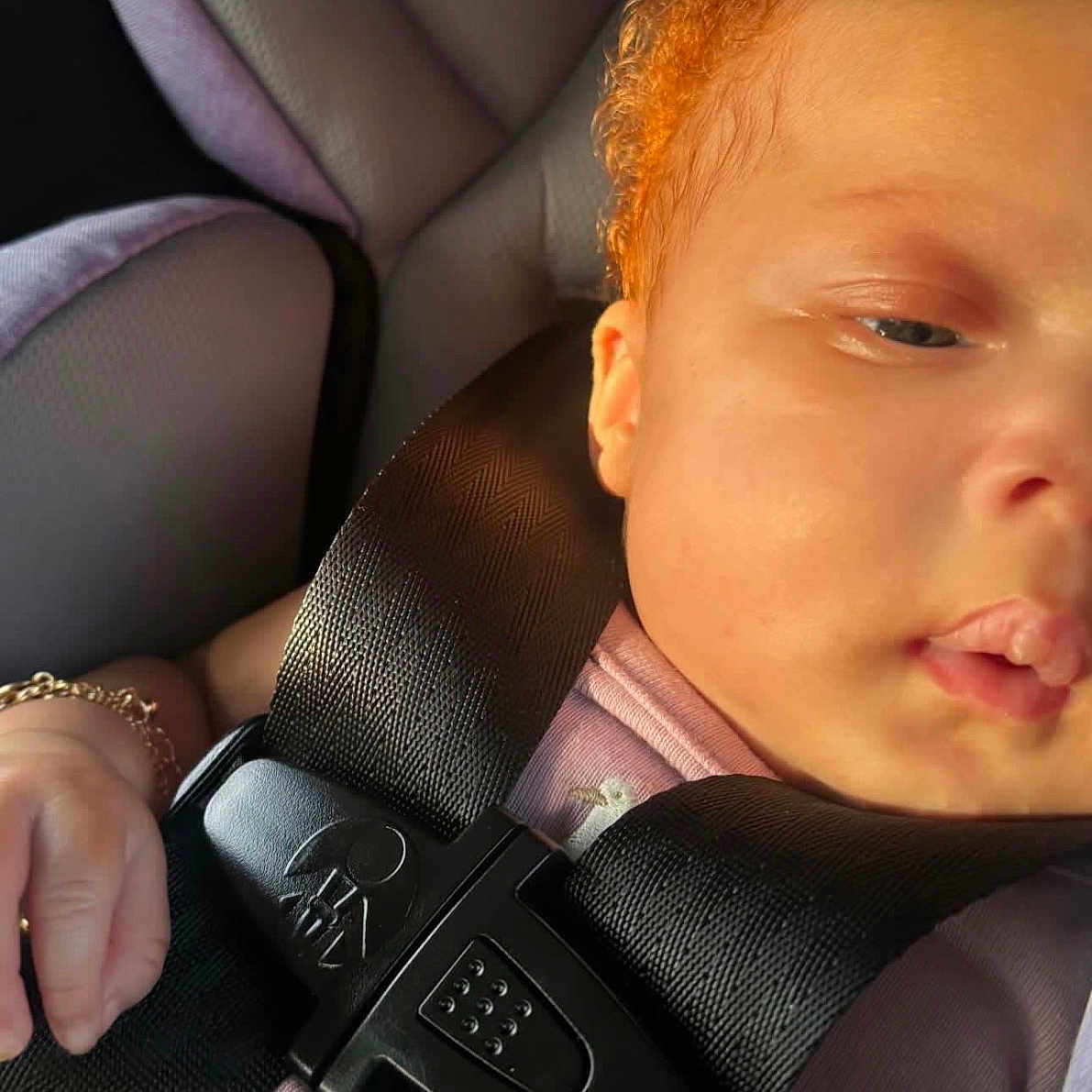 Syomii is registered to the contest to win money with this photo: baby, car_seat, child, child_safety, closeup, curly_hair, hand, harness, infant, pink_clothing, portrait, relaxed, safety, seat, seatbelt, skin, sleepy, sunlight, transportation, young_child
