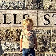 Jaden is registered to the contest to win money with this photo: blond_hair, casual_clothing, child, concrete, daylight, engraved_text, jeans, outdoor, person, portrait, shadow, sidewalk, smiling, sneakers, standing, stone_wall, sunlight, toddler, tshirt, young_child