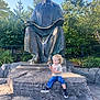 Jaden joined the competition — help win amazing prizes! bronze_statue, child, curly_hair, daytime, greenery, jeans, nature, outdoor, park, person, reading, rock, sculpture, shoes, sitting, statue, sunlight, toddler, trees, tshirt