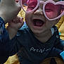 baby, child, glasses, pink_sunglasses, heart_shaped, smiling, laughing, hand, indoor, clothing, person, cute, happy, playful, joy, face, head, seated, toy, cozy