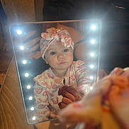 Brooklyn is registered to the contest to win money with this photo: baby, child, cozy, cute, expression, face, hand, headband, home, indoor, lights, mirror, pajamas, person, portrait, rainbow_pattern, reflection, sitting, soft_focus, warm_lighting