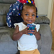 Jannah joined the competition — help win amazing prizes! toddler, child, smiling, indoor, sofa, cup, backpack, hair_beads, white_shirt, yellow_pants, carpet, earrings, furniture, home, happy, person, portrait, young_child, seated, casual_clothing
