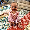 baby, baby_swing, barefoot, blanket, child, couch, face, happy, home, indoor, infant, living_room, onesie, patterned_textile, pink_clothing, play_area, portrait, quilt, sitting, smiling