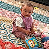 Aurorabelle is registered to the contest to win money with this photo: baby, bib, blanket, carpet, child, curious, face, home_decor, indoors, infant, looking_at_camera, patterned_fabric, pink_clothing, playroom, plush_toy, portrait, quilt, sitting, stuffed_animal, toy_book