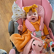 Eva-Willow is registered to the contest to win money with this photo: baby, child, smiling, stroller, pink, yellow, headband, bow, blanket, plush_toy, toy, happy, indoor, clothing, seat_belt, wood_floor, person, cute, infant, comfort